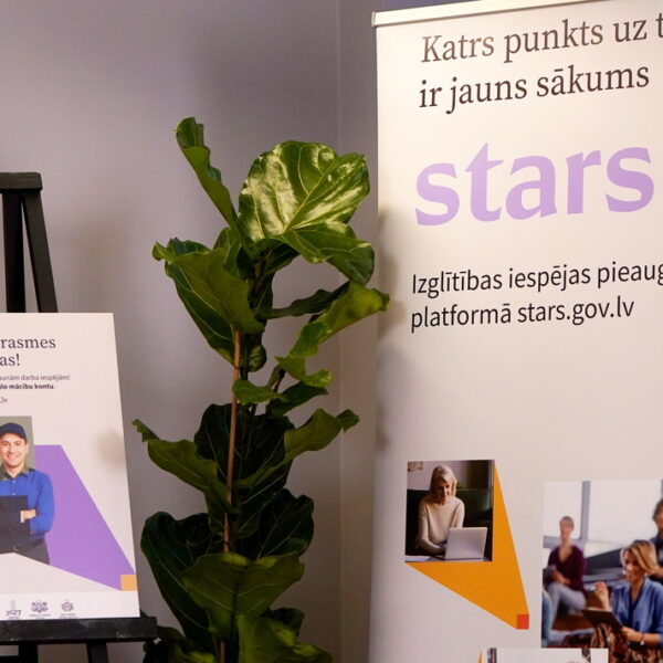 Divi plakāti reklamē izglītības platformu pieaugušajiem "stars.gov.lv". Kreisais plakāts ar uzrakstu "Atjaunini prasmes un zināšanas!" attēlo smaidīgu vīrieti un tekstu "Virzies pretī izaugsmei vai jaunām darba iespējām! Lai sāktu, izveido individuālo mācību kontu. Uzzini vairāk: stars.gov.lv". Labais plakāts, kurā lieli burti veido vārdu "stars", satur uzrakstus "Katrs punkts uz taisnes ir jauns sākums" un "Izglītības iespējas pieaugušajiem platformā stars.gov.lv", kā arī attēlus ar cilvēkiem, kas mācās vai strādā ar datoru. Starp plakātiem stāv liels zaļš telpaugs.